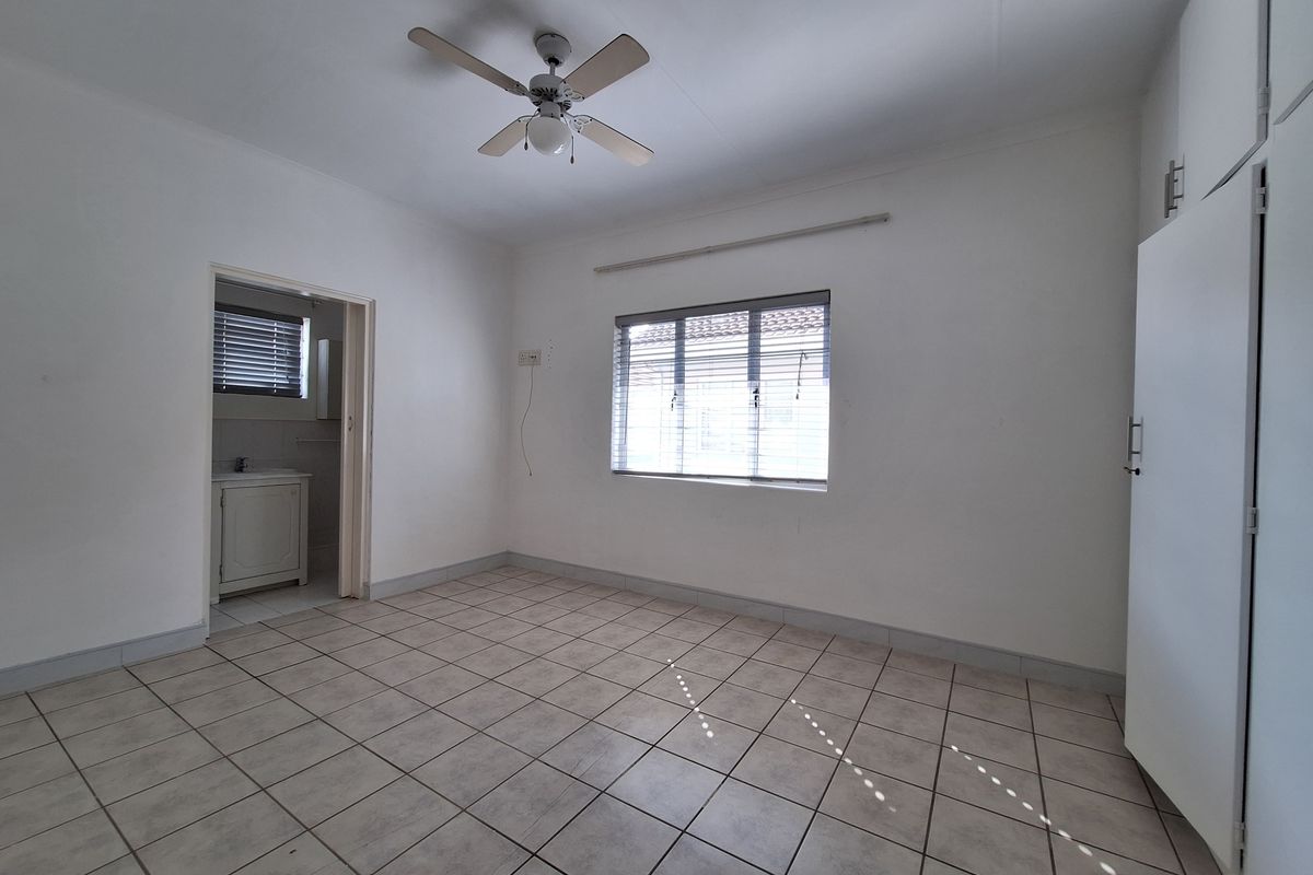 A spacious bedroom featuring tiled flooring, a ceiling fan, and built-in cupboards, with an adjoining en-suite bathroom.