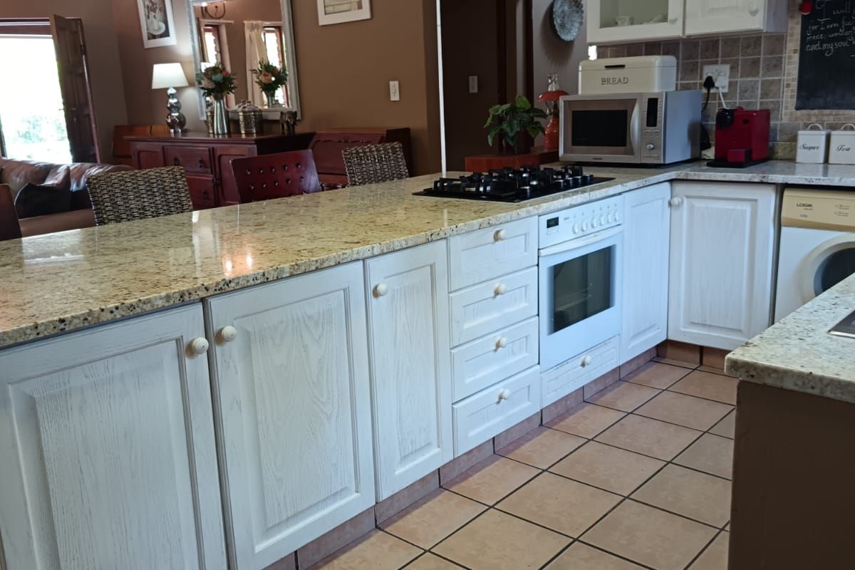 A functional kitchen featuring granite countertops, white cabinetry, a built-in oven, and gas hob, seamlessly flowing into the adjacent living area.
