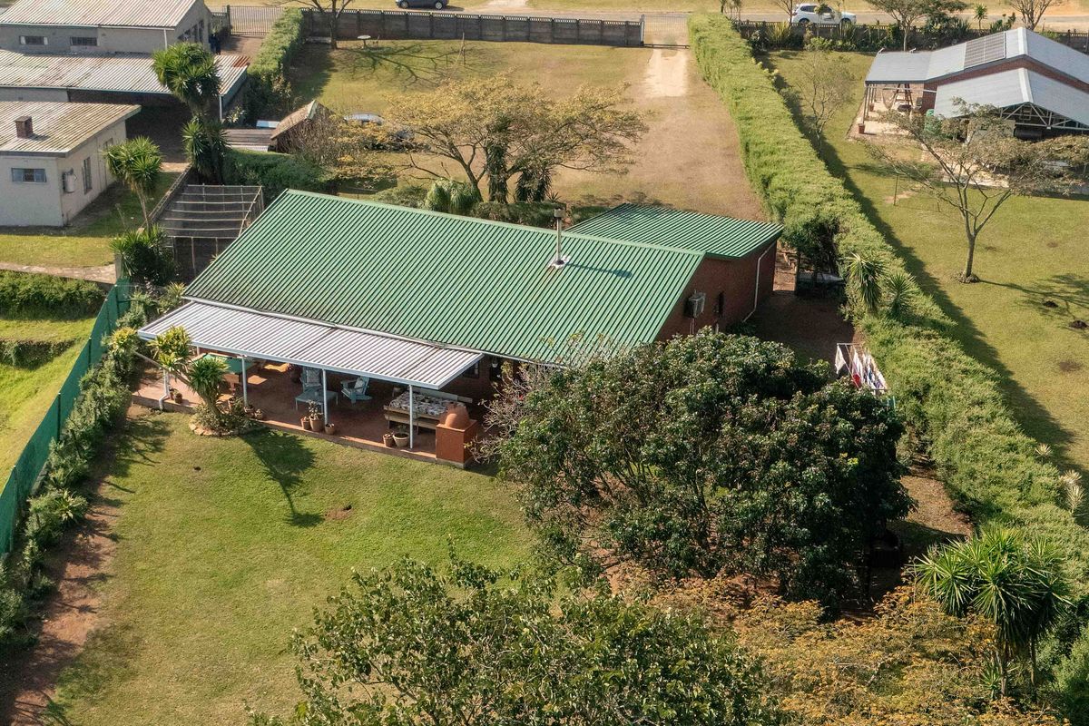 Aerial view of a residential property featuring a green metal roof, a covered patio area, and a spacious garden within a fenced plot.