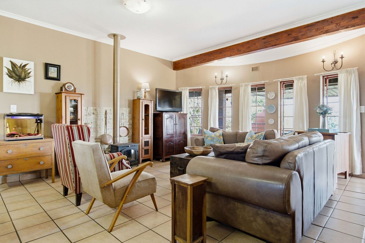 Spacious living room featuring a wood-burning fireplace with stone surround, exposed timber ceiling beams, and neutral tiled flooring.