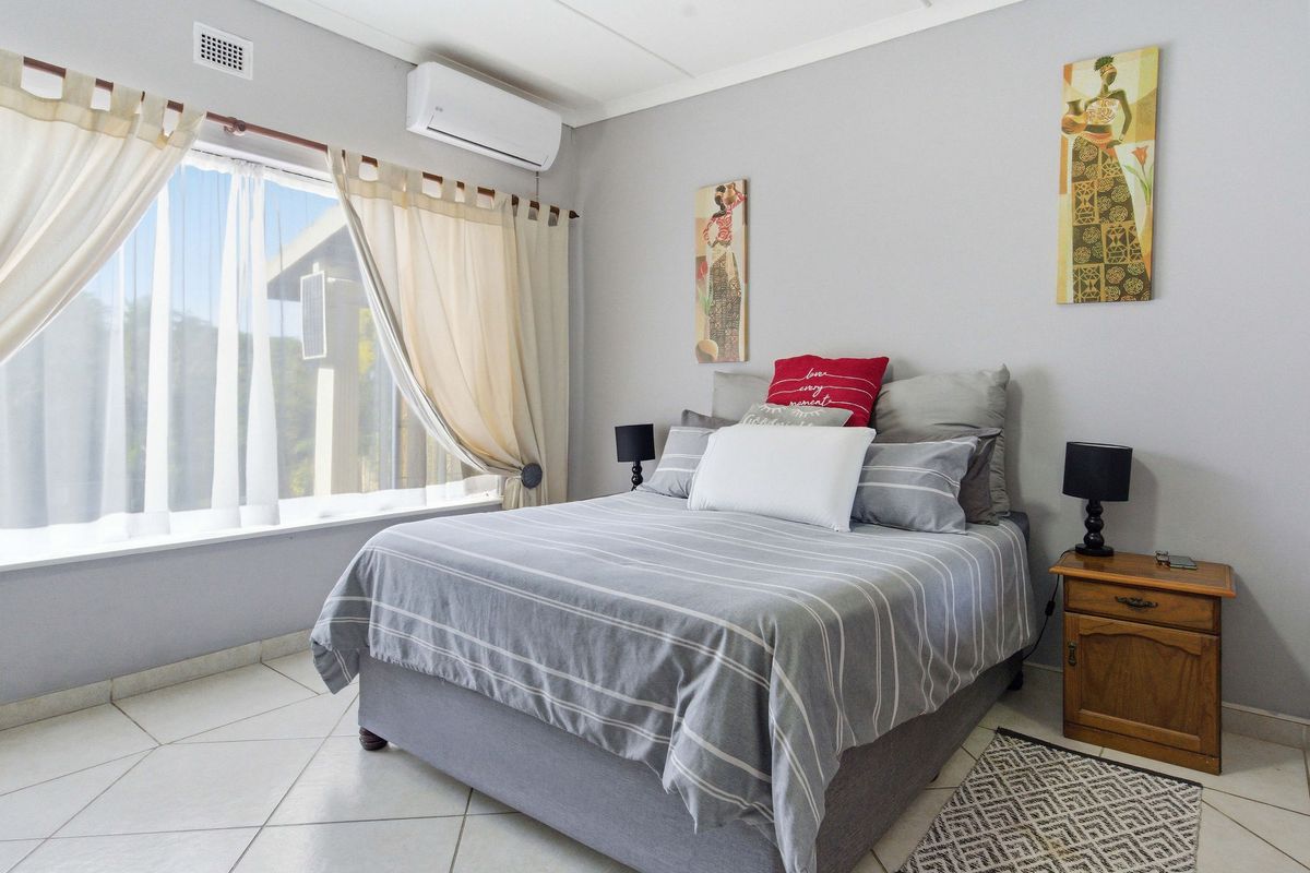 A well-maintained bedroom featuring tiled flooring, a wall-mounted air conditioning unit, and large windows allowing for natural light.