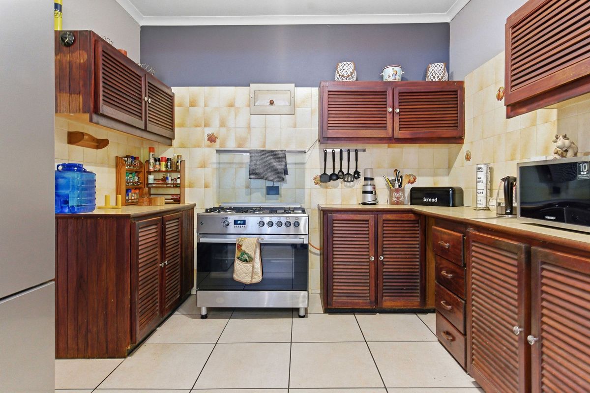 A functional kitchen featuring wooden louvered cabinetry, tiled splashbacks, and a freestanding gas stove with an integrated extractor fan.
