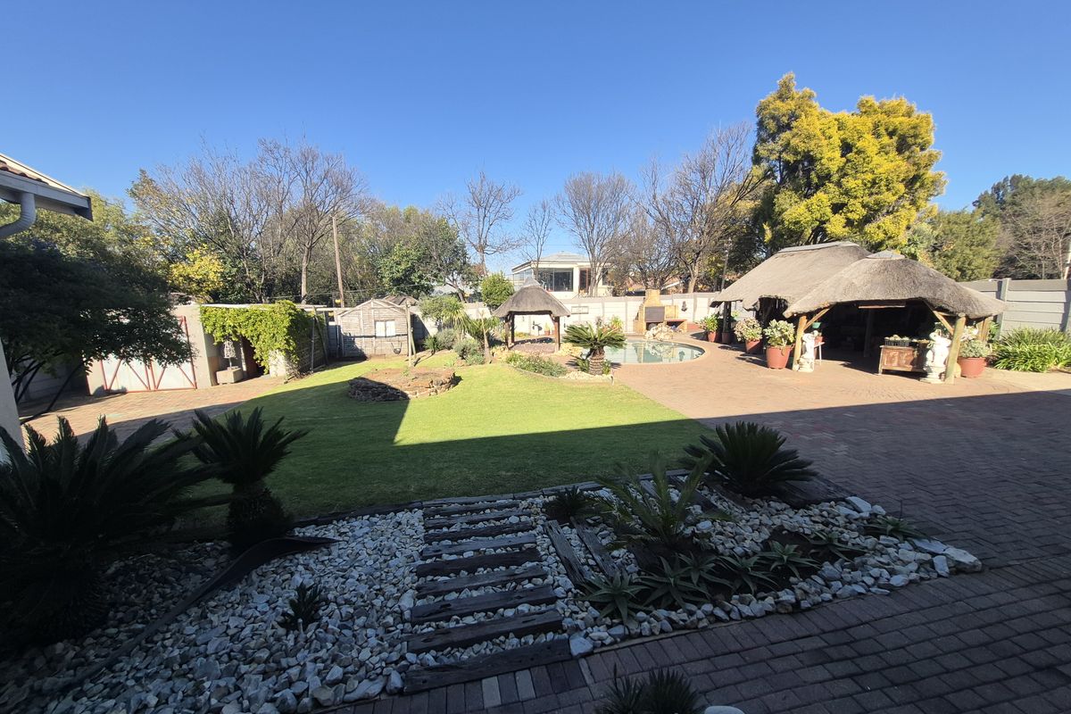 Spacious rear garden featuring a swimming pool, paved entertainment area, and a traditional thatch lapa, ideal for outdoor living and recreation.
