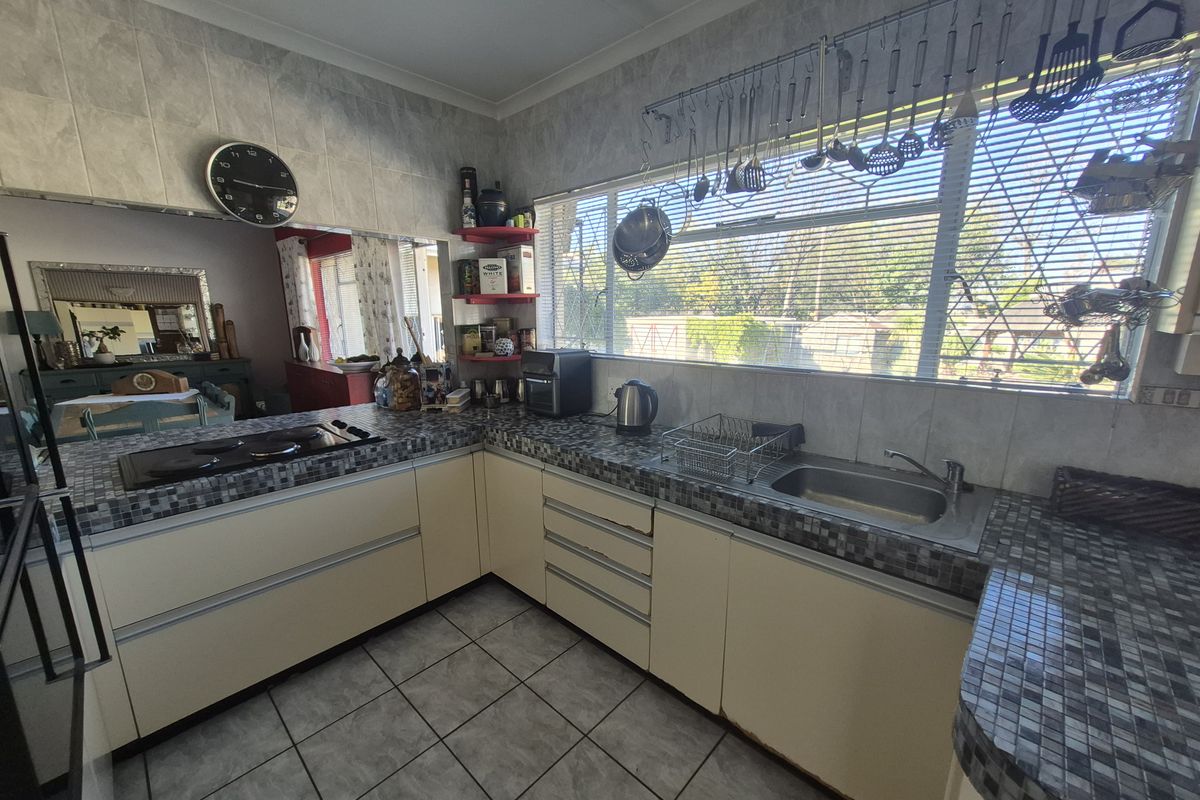A functional kitchen featuring mosaic tiled countertops, built-in cabinetry, a stainless steel sink, and a built-in hob, with large windows providing natural light.