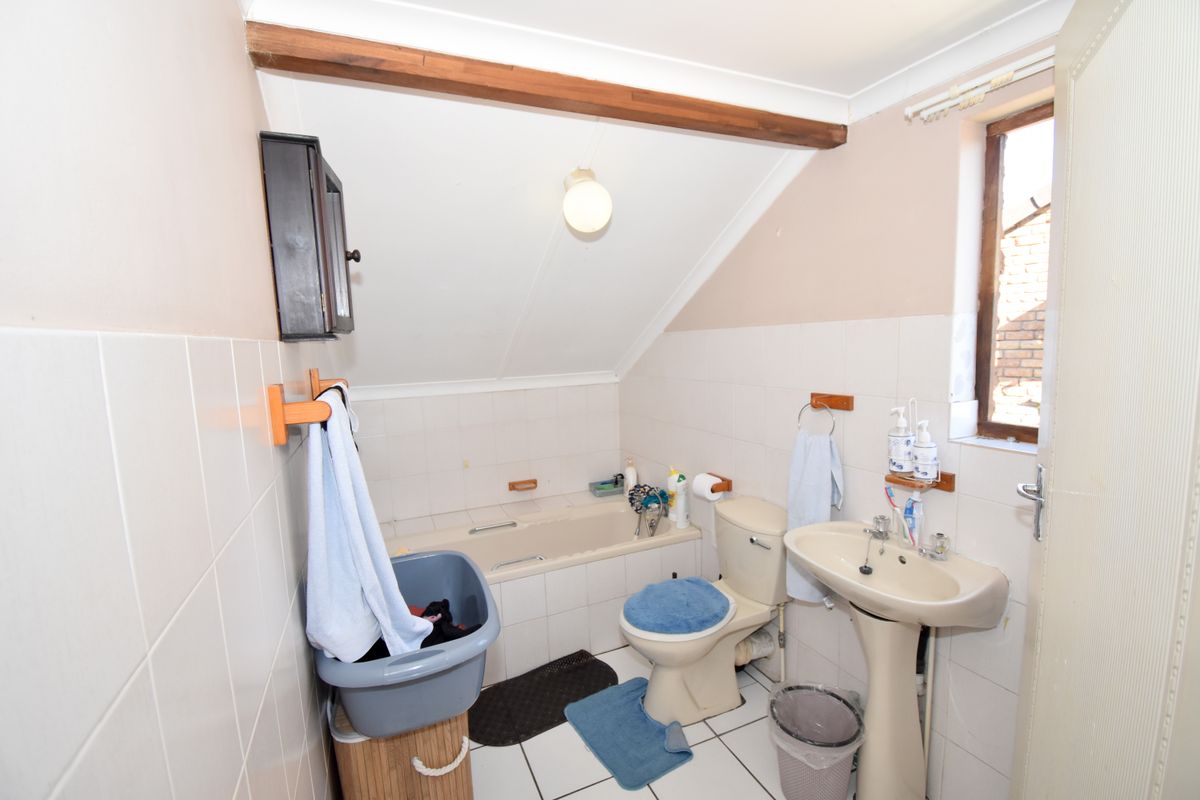A compact bathroom featuring a bathtub, pedestal sink, and toilet, finished with tiled walls and flooring under an exposed timber beam.
