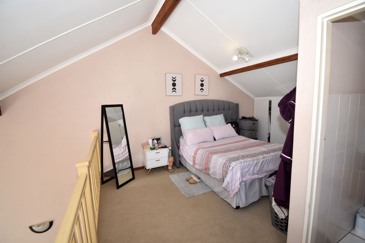 A cozy loft-style bedroom featuring a vaulted ceiling with exposed timber beams and a timber balustrade overlooking the lower level.