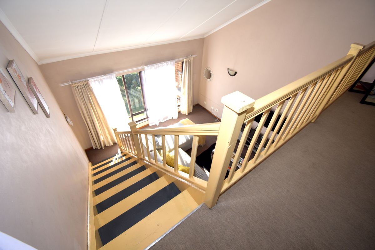 View from the upper landing looking down into a living area featuring a staircase with a wooden balustrade and access to a patio.