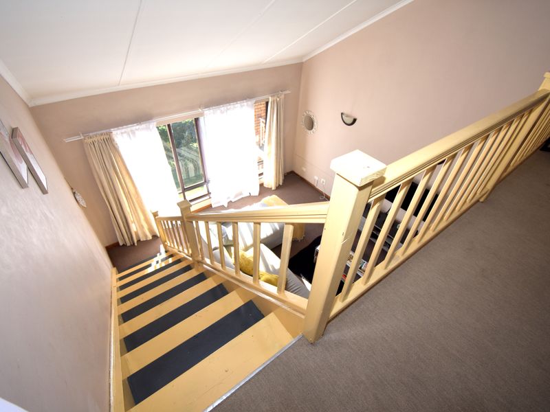 View from the upper landing looking down into a living area featuring a staircase with a wooden balustrade and access to a patio.