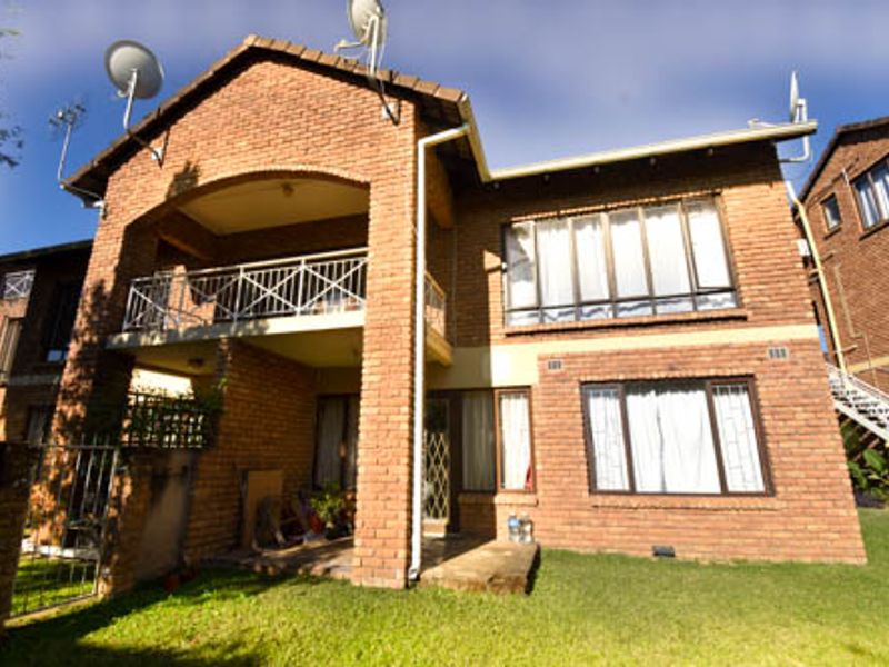 Rear view of a double-story face brick apartment building featuring a balcony, large windows, and a small private garden area.