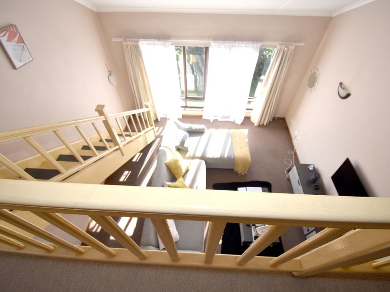 An elevated view looking down into a living room featuring a timber staircase, balustrade, and large window allowing natural light.
