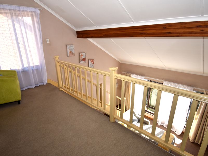 A mezzanine hallway area featuring a timber balustrade, exposed wooden beam, and sloped ceilings overlooking the lower level.