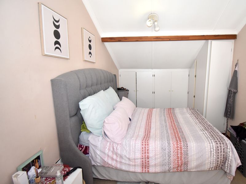 A cozy bedroom featuring a sloped ceiling, exposed timber beam, and ample built-in cupboard storage.