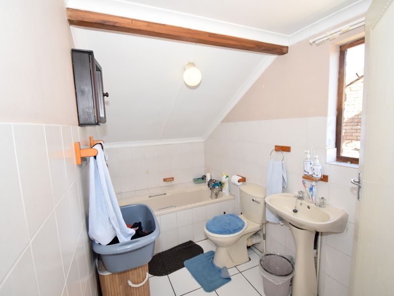A compact bathroom featuring a bathtub, pedestal sink, and toilet, finished with tiled walls and flooring under an exposed timber beam.