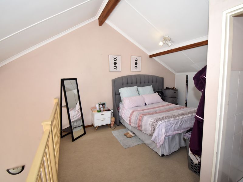 A cozy loft-style bedroom featuring a vaulted ceiling with exposed timber beams and a timber balustrade overlooking the lower level.