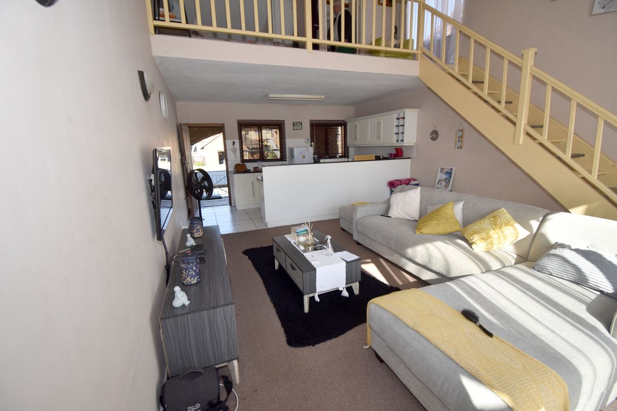 Open-plan living area featuring a mezzanine level with a timber staircase, integrated kitchen space, and direct access to an exterior area.