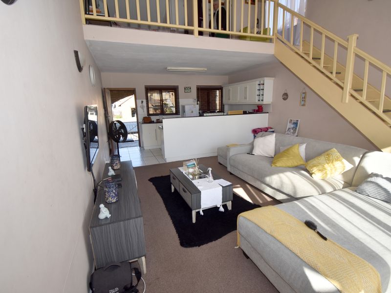 Open-plan living area featuring a mezzanine level with a timber staircase, integrated kitchen space, and direct access to an exterior area.