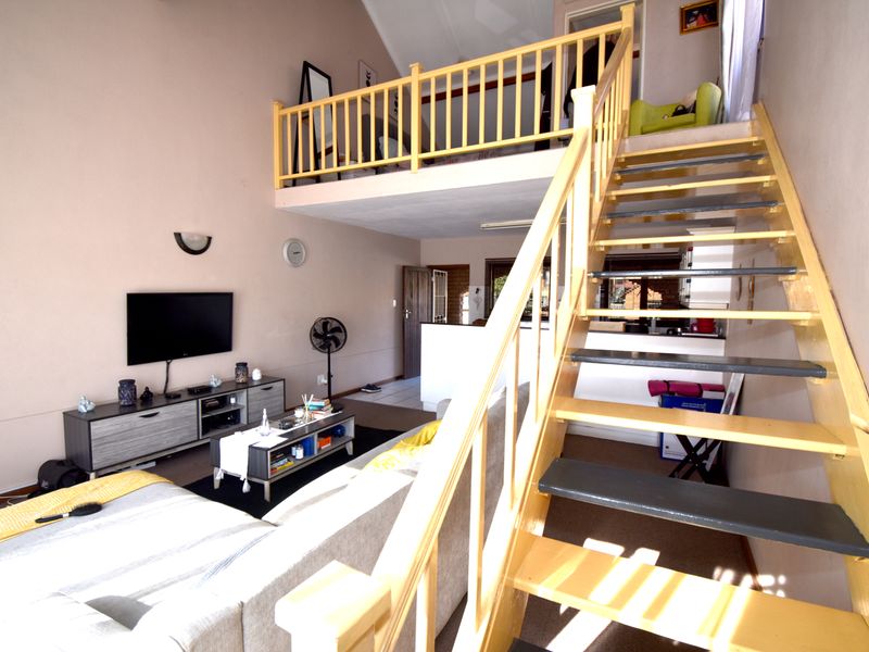 Open-plan living area featuring a vaulted ceiling and a timber staircase leading to a mezzanine level.