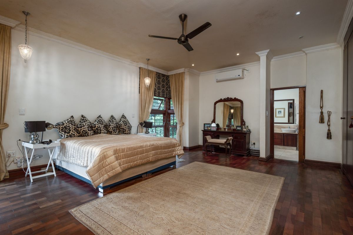Spacious bedroom featuring dark hardwood flooring, crown molding, ceiling fan, and an en-suite bathroom access.