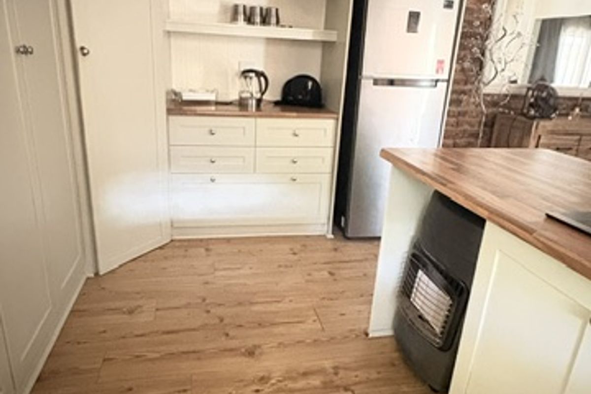 A well-maintained kitchen featuring exposed brick walls, timber flooring, and custom built-in cabinetry with open shelving and a butcher block countertop.