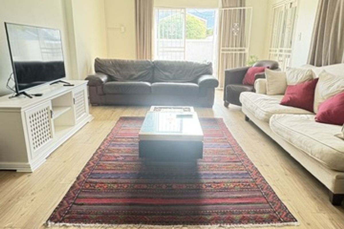 Spacious living room featuring light wood-look laminate flooring, a decorative ceiling rose with a chandelier, and sliding glass doors leading to the exterior.