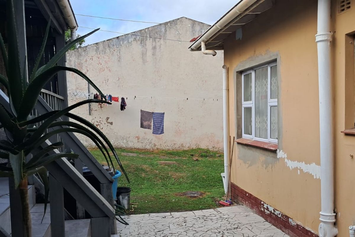 Rear exterior view showing a paved patio area, timber staircase, and weathered exterior walls requiring maintenance.