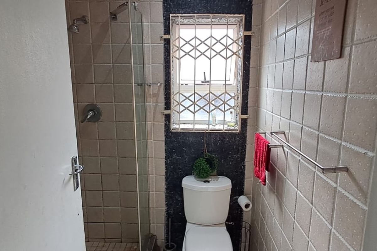 A compact bathroom featuring a shower with a glass screen, toilet, and tiled walls with security bars on the window.