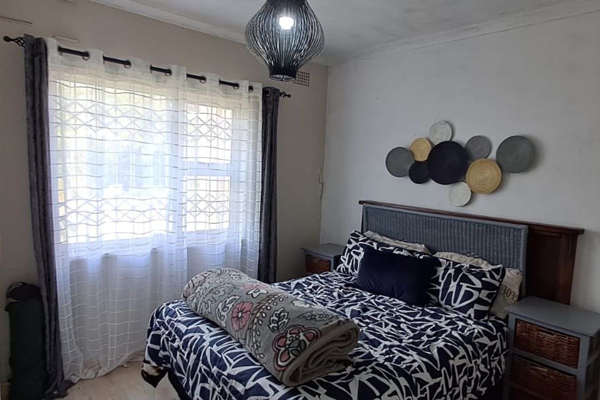 A functional bedroom featuring a window with a security gate and a built-in headboard, offering a comfortable space with potential for cosmetic updates.