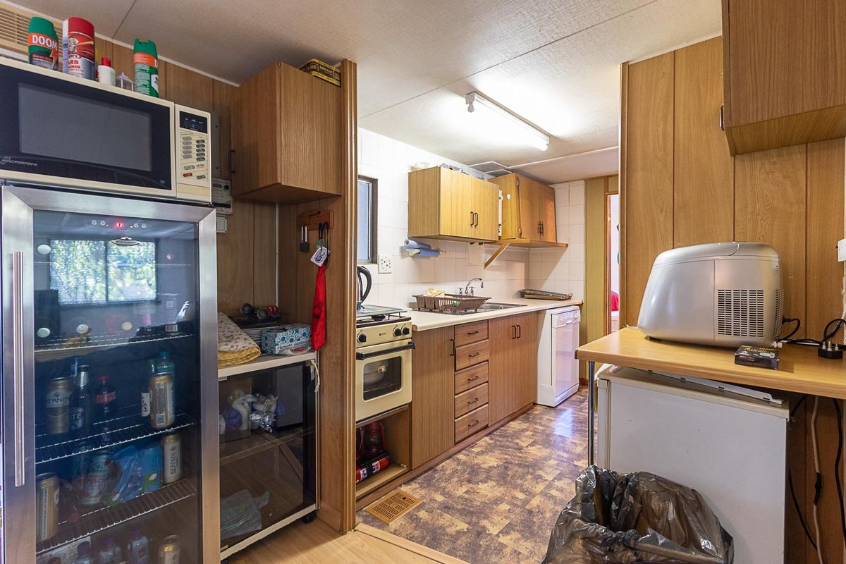 A compact, dated kitchen featuring wood-look cabinetry, laminate countertops, a built-in oven, and a stainless steel sink, requiring modernization.