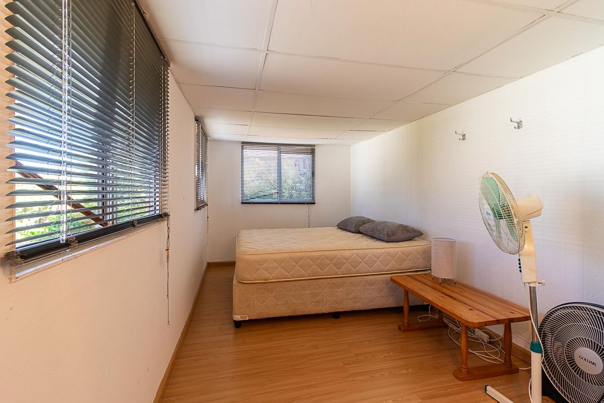A simple bedroom featuring laminate flooring, venetian blinds, and a drop ceiling, offering a functional space with potential for modernization.