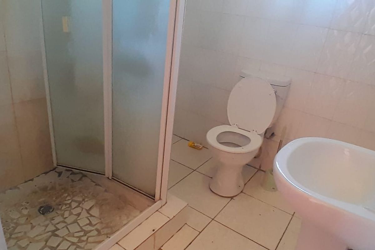 A functional bathroom featuring a corner shower enclosure, a pedestal sink, and a standard toilet with white tiled walls and flooring.