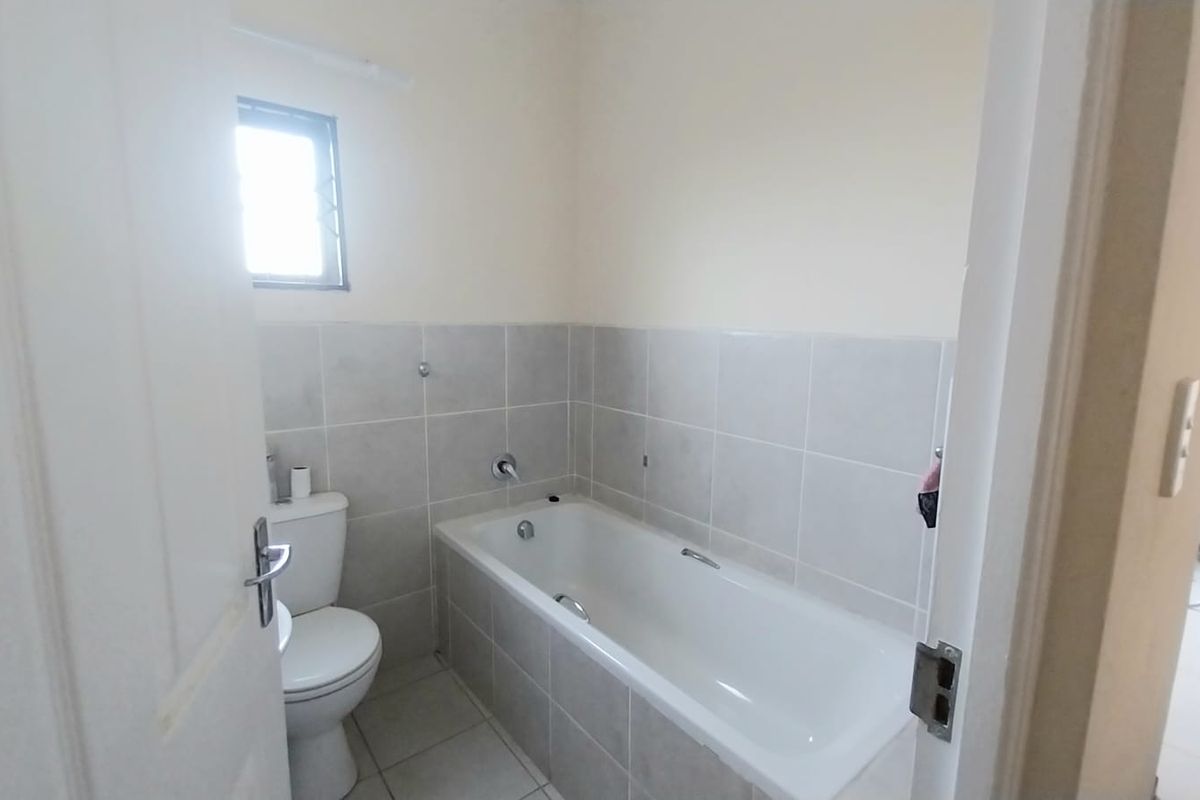A functional bathroom featuring a bathtub, toilet, and neutral wall tiling, offering a clean and simple layout.