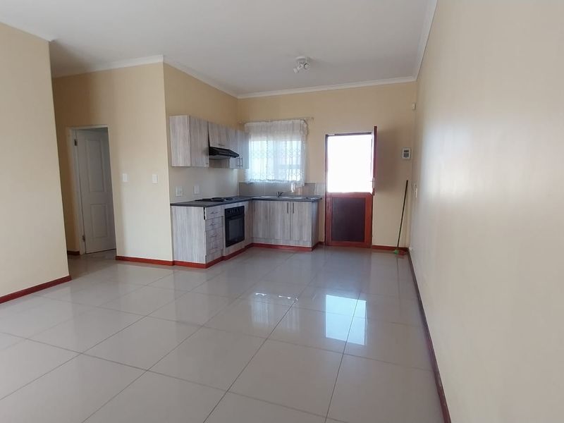 An open-plan living and kitchen area featuring tiled flooring, neutral walls, and built-in kitchen cabinetry with an integrated oven and hob.