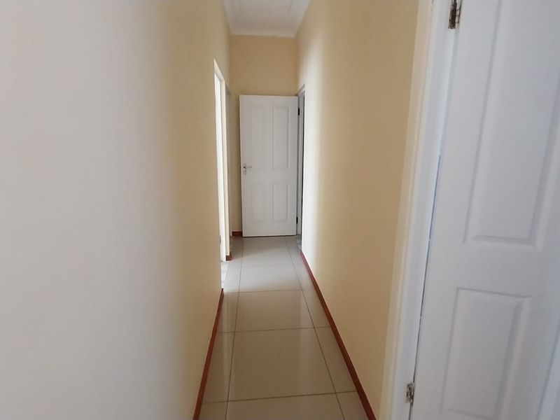 A clean and simple interior hallway featuring neutral wall tones, tiled flooring, and multiple internal doors providing access to adjacent rooms.