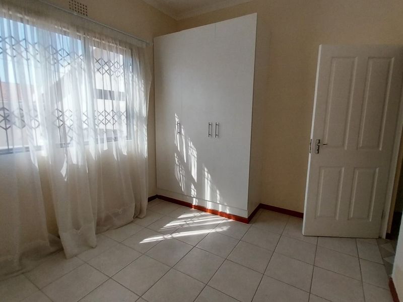 A bright, empty bedroom featuring tiled flooring and a built-in white wardrobe, offering a clean and neutral space ready for personalization.