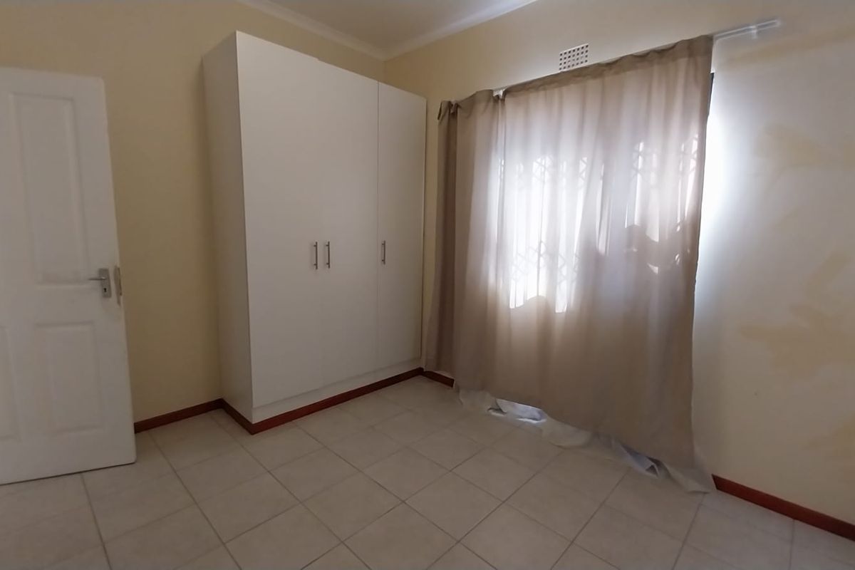 A vacant bedroom featuring tiled flooring, a built-in wardrobe, and a window fitted with a security gate.