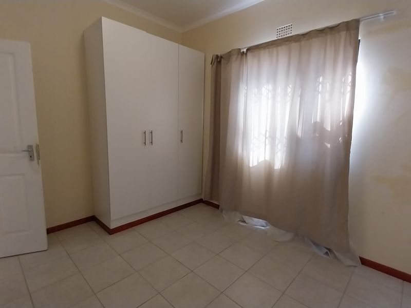 A vacant bedroom featuring tiled flooring, a built-in wardrobe, and a window fitted with a security gate.