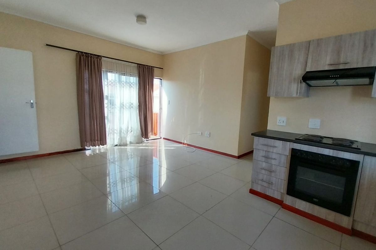 Open-plan living area featuring tiled flooring and a compact kitchen equipped with a built-in oven, hob, and extractor fan.