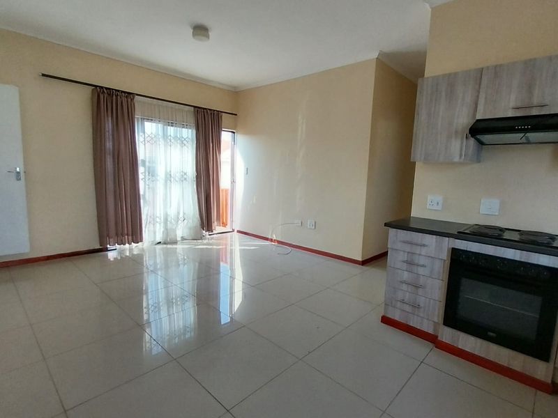 Open-plan living area featuring tiled flooring and a compact kitchen equipped with a built-in oven, hob, and extractor fan.