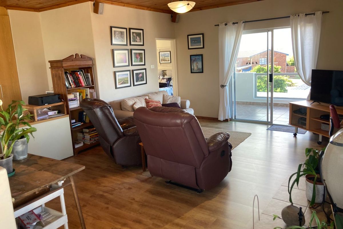 A comfortable living room featuring timber ceiling paneling, laminate flooring, and a sliding glass door providing access to an outdoor balcony area.