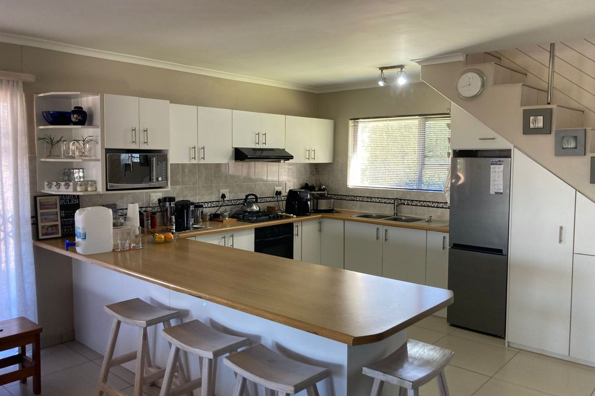 Functional kitchen featuring white cabinetry, laminate countertops, a breakfast bar, and integrated appliances, with an adjacent staircase.