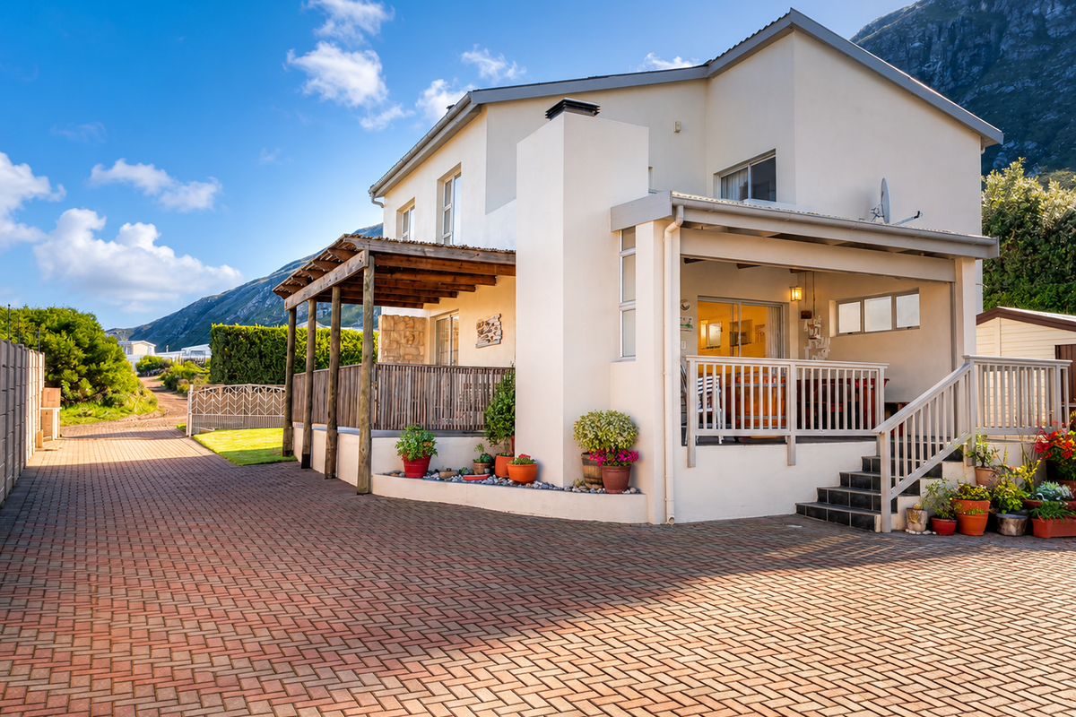 A well-maintained rear exterior view featuring a paved driveway, timber pergola, elevated deck, and a covered patio area with mountain views.