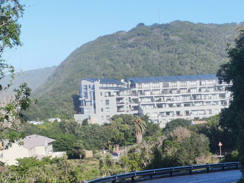 A scenic view of a multi-story apartment complex nestled against a lush, green mountain backdrop.