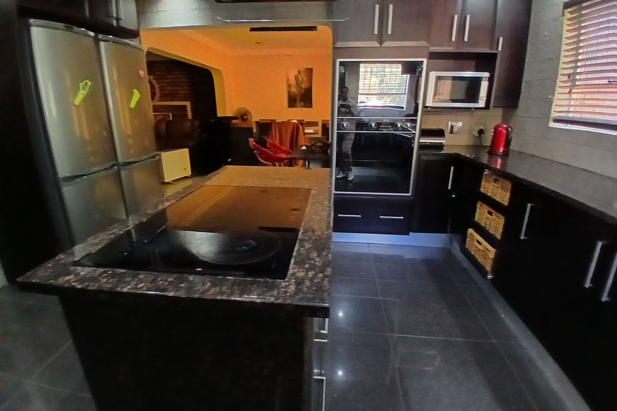 A functional kitchen featuring dark wood cabinetry, granite countertops, a central island with an integrated hob, and built-in oven and microwave appliances.