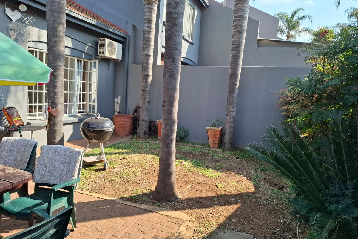 Rear garden area featuring a paved patio, boundary wall, and established palm trees, providing a private outdoor space for the townhouse.