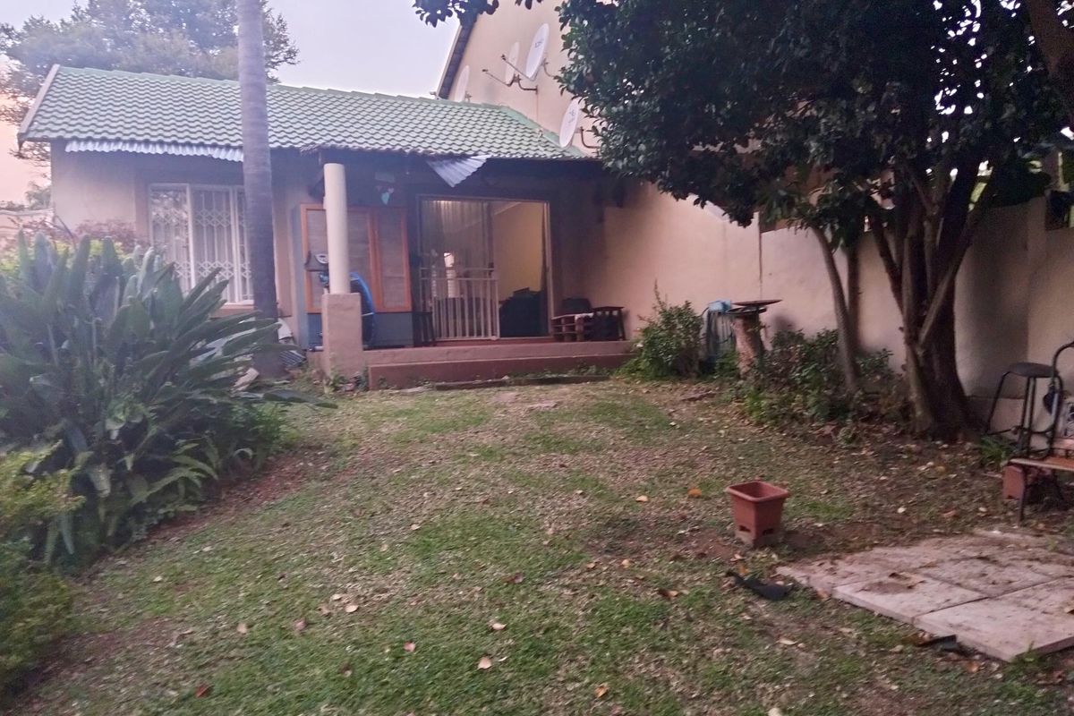 Rear view of the townhouse featuring a small garden, a covered patio area, and a sliding door entrance.