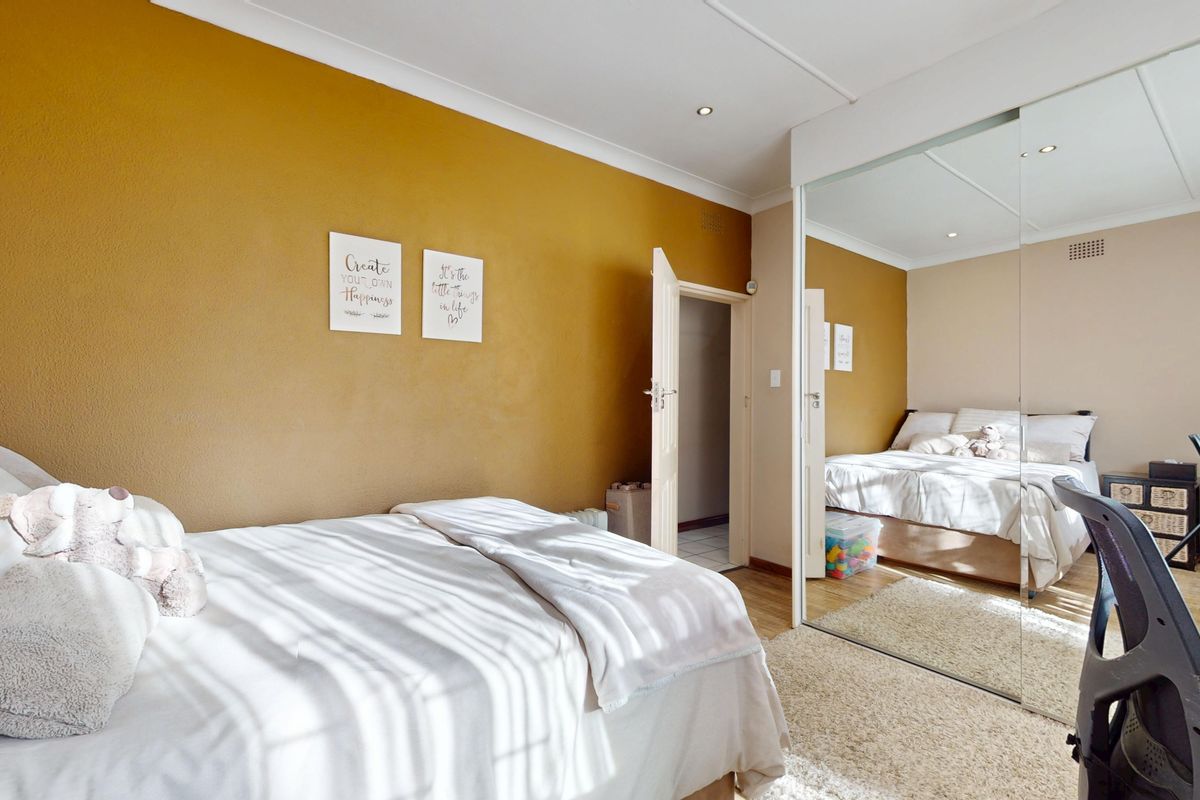 A bedroom featuring a mustard accent wall, recessed downlighting, and a large built-in mirrored wardrobe with an adjoining walk-in closet.