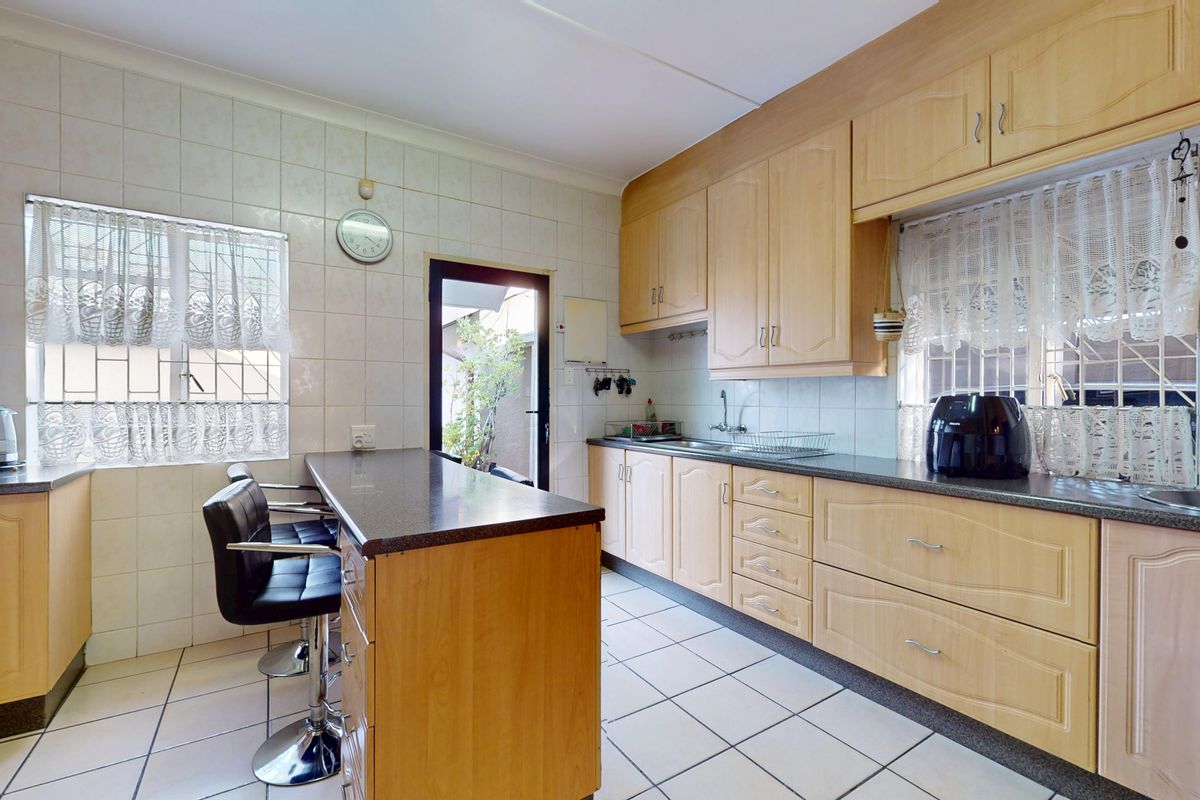 A functional kitchen featuring light wood-tone cabinetry, dark laminate countertops, tiled splashbacks, and a breakfast bar area with direct access to the exterior.
