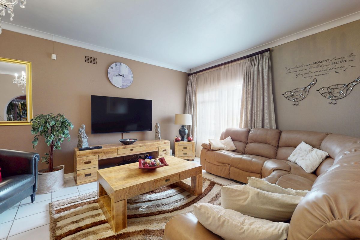 A comfortable living room featuring tiled flooring, coving, and large windows with curtain tracks, providing a functional and well-lit space.