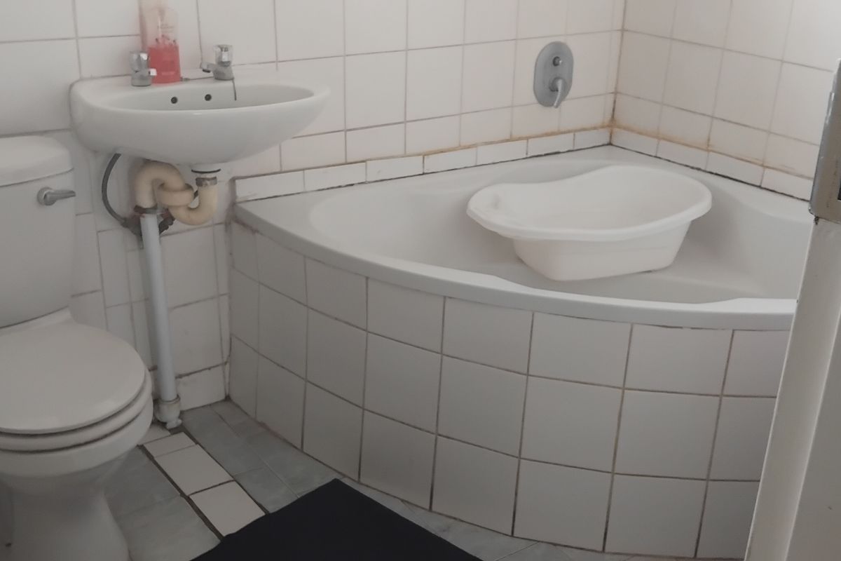 A compact bathroom featuring a corner bathtub, wall-mounted basin, and toilet with white ceramic wall tiling throughout.