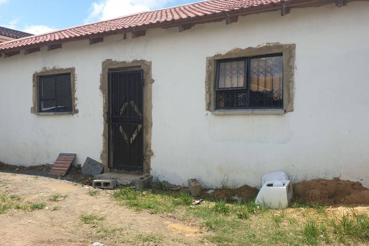 Exterior view of a house facade featuring security gates and window bars, currently showing unfinished plastering and exterior maintenance requirements.